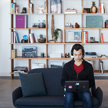individual working on laptop headphones bookshelf behind