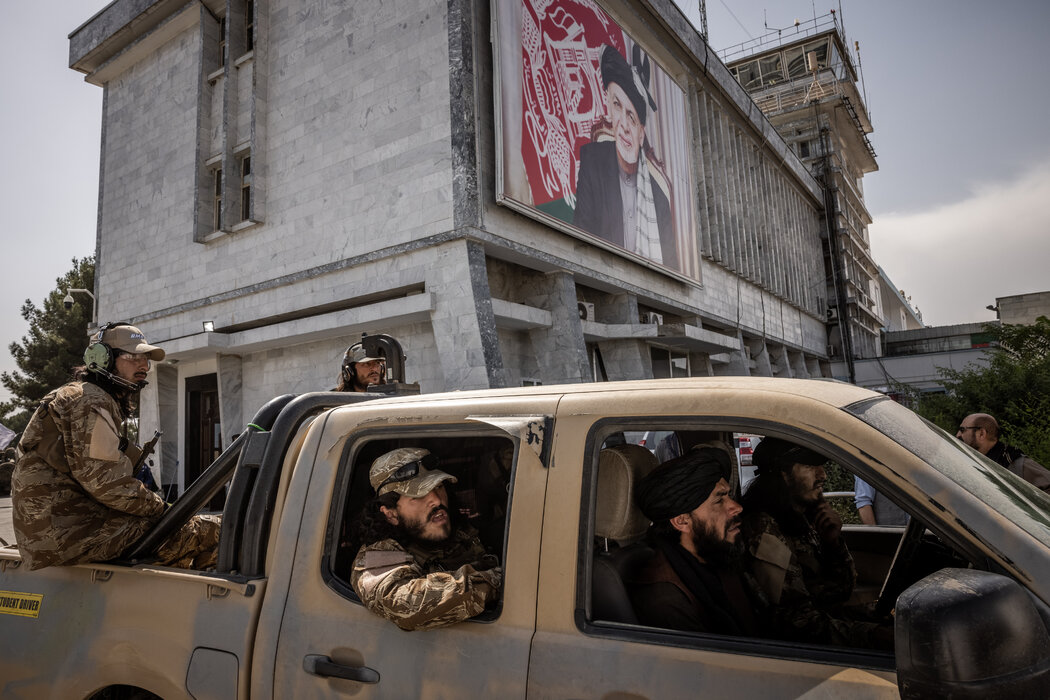 周四,塔利班武装分子在喀布尔机场驶过前总统阿什拉夫·加尼的宣传画。