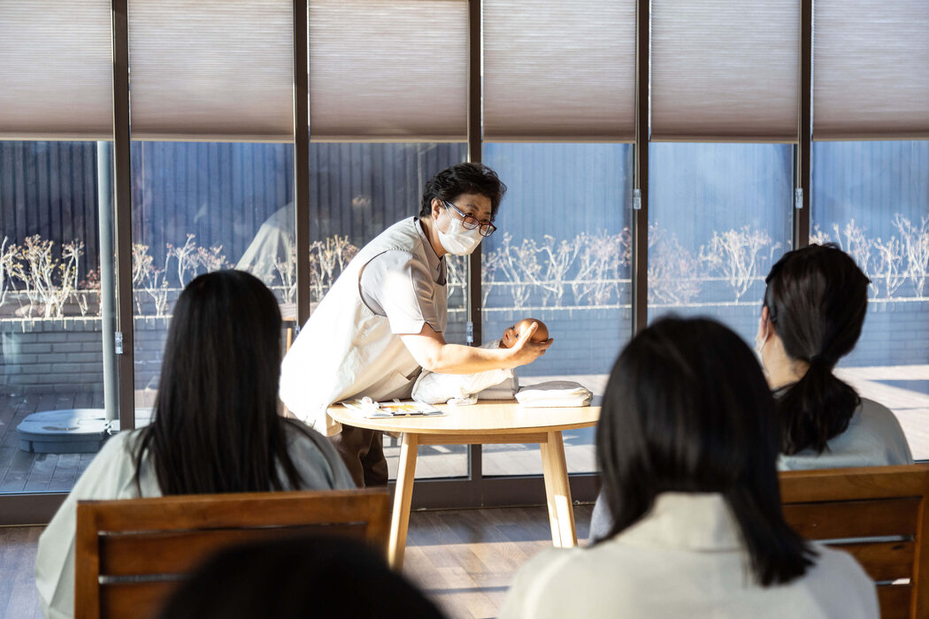 St. Park的护士长李姝贝(音)在婴儿护理班上向身着统一睡袍的妈妈们讲解如何抱婴儿和让婴儿打嗝。